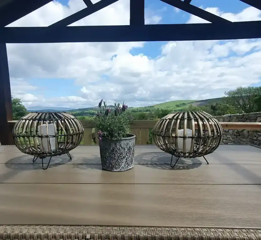 2 metal wire and leg lanterns. a small purple colour flower plant in a flower pot between the 2 lanterns. A clear sunny sky at the background